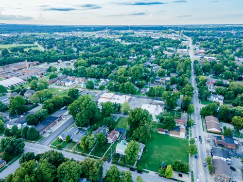 Aerial view of a small town with green trees, residential areas, and roads stretching into the distance.