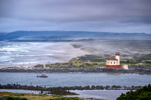 A coastal scene featuring a lighthouse, a boat on the water, and misty hills in the background.
