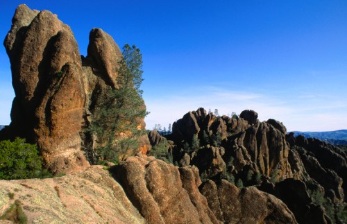 Rocky formations rise against a clear blue sky, with scattered trees dotting the landscape.