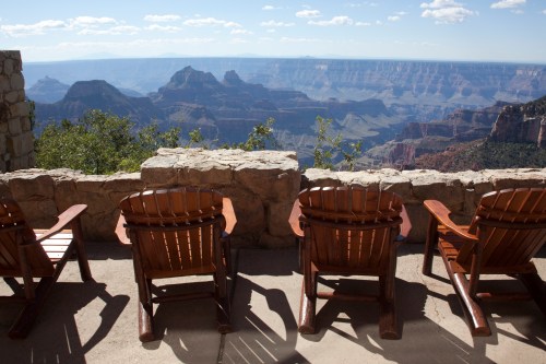 Four wooden chairs overlook a stunning view of the Grand Canyon, with mountains and blue sky in the background.