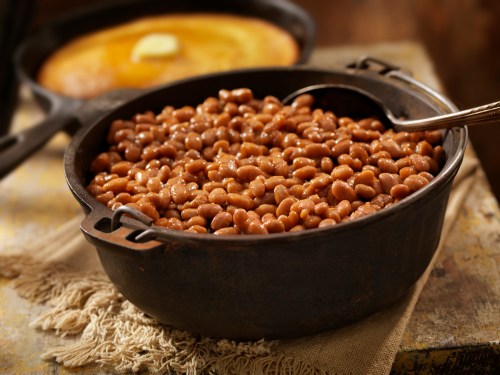 A cast iron pot filled with cooked pinto beans, with a spoon resting inside, on a rustic table.