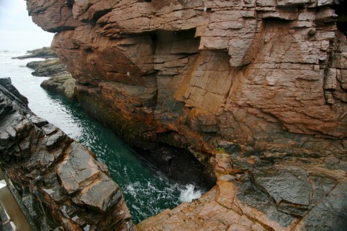 Rocky cliffs frame a narrow inlet with turquoise water, creating a dramatic coastal landscape.