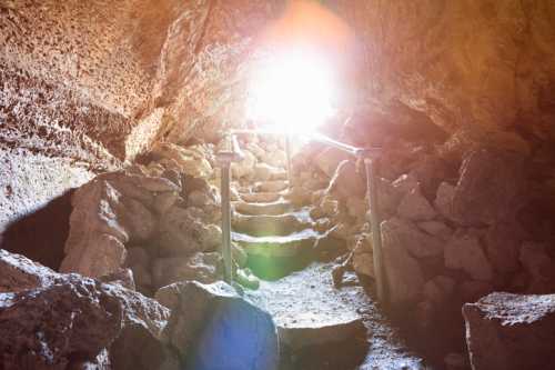 A rocky cave entrance with steps leading up to bright light, surrounded by rough stone walls.