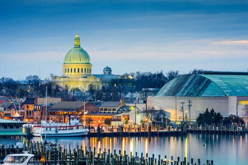 A scenic view of a harbor at dusk, featuring a dome building and a large structure, with boats docked along the waterfront.