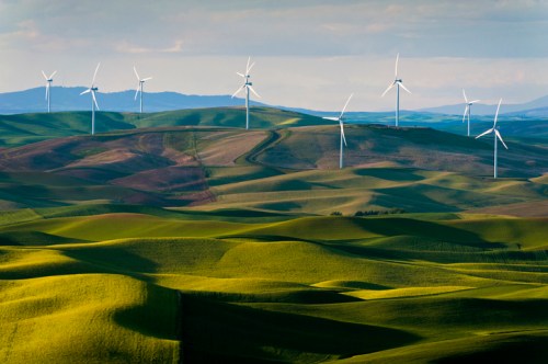 A scenic landscape featuring rolling green hills and several wind turbines against a blue sky.