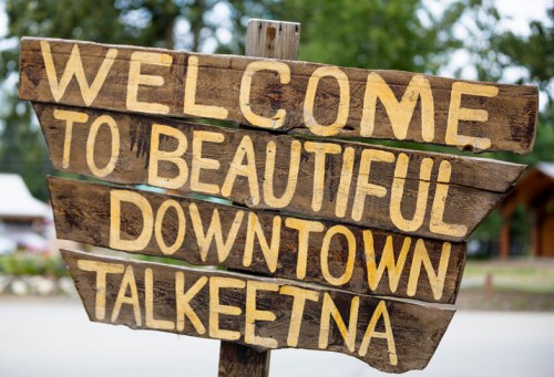 Wooden sign reading "Welcome to Beautiful Downtown Talkeetna" with a rustic design and natural background.