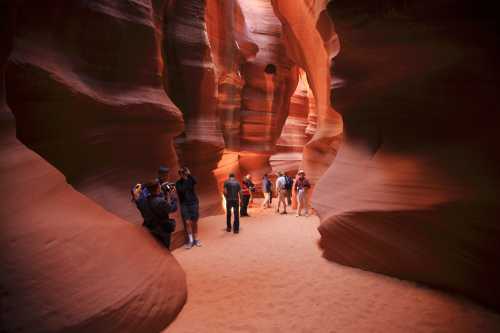 Visitors explore the narrow, winding passage of a sandstone canyon illuminated by warm, natural light.