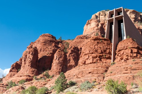 A modern building stands against a backdrop of red rock formations under a clear blue sky.