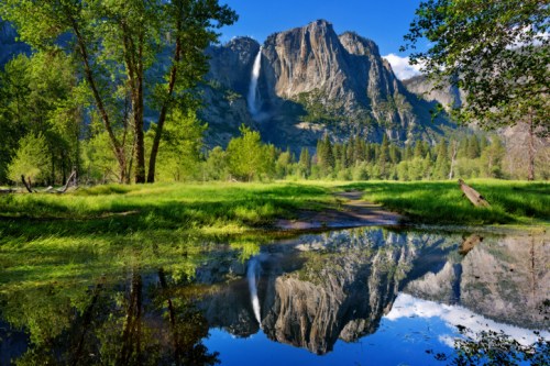 A serene landscape featuring a waterfall cascading down a mountain, surrounded by lush greenery and a reflective pond.