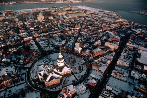 Aerial view of a snow-covered city with a circular building at the center, surrounded by streets and waterfront.