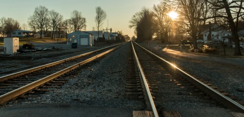 A tranquil scene of railway tracks stretching into the distance, with a sunset illuminating the landscape.