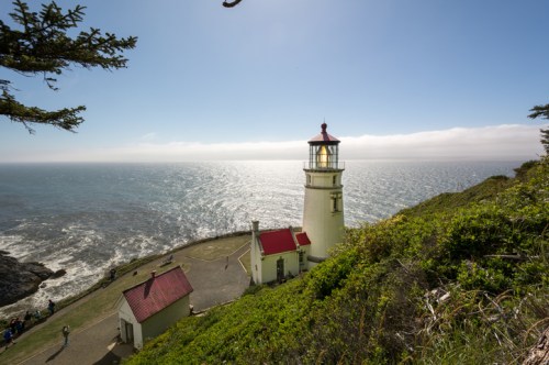 A scenic view of a lighthouse on a cliff overlooking the ocean, surrounded by greenery and a clear blue sky.