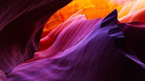 Vibrant, swirling rock formations in shades of purple, orange, and red, illuminated by warm light in a canyon.