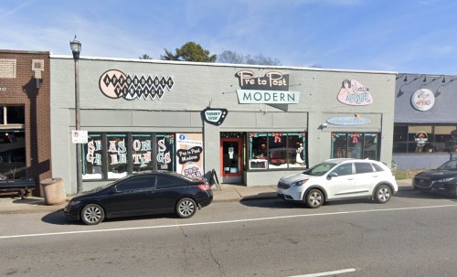 A storefront labeled "Pre to Post Modern" with various signs, parked cars, and a sidewalk in a commercial area.