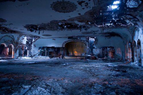 A dilapidated interior of a large, abandoned building with crumbling walls and debris scattered across the floor.