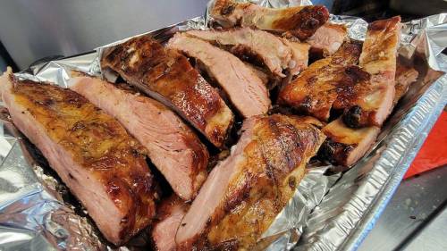 A tray of succulent, grilled pork ribs with a caramelized glaze, arranged neatly on aluminum foil.