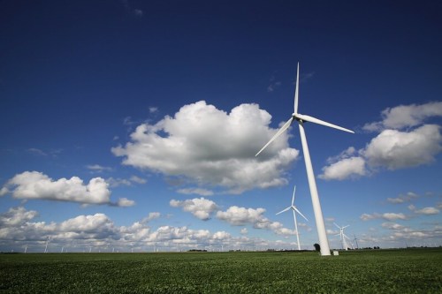 A landscape featuring wind turbines against a blue sky with fluffy clouds and green fields.