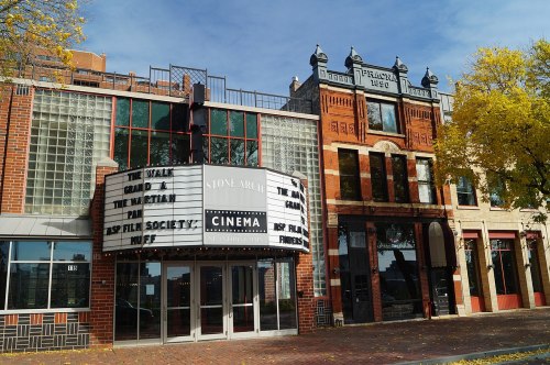 A historic cinema building with a marquee displaying movie titles, surrounded by brick architecture and autumn trees.