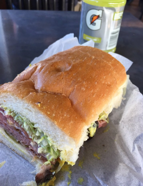 A close-up of a sandwich with layers of meat and lettuce, next to a bottle of Gatorade on a table.