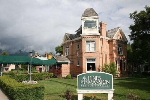 Historic Hines Mansion with a green lawn, sign, and cloudy sky in the background.