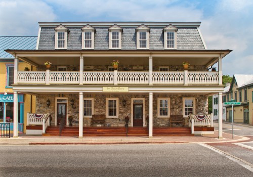 Historic stone building with a large porch, multiple windows, and decorative flower boxes, set in a quaint town.