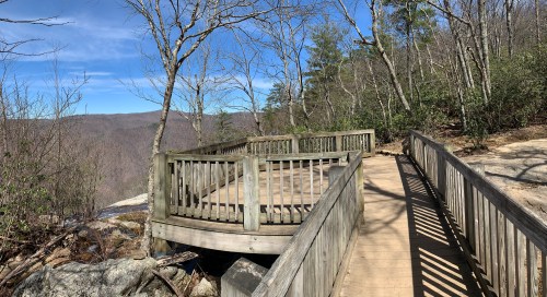 A wooden observation deck surrounded by trees, overlooking a scenic valley under a clear blue sky.