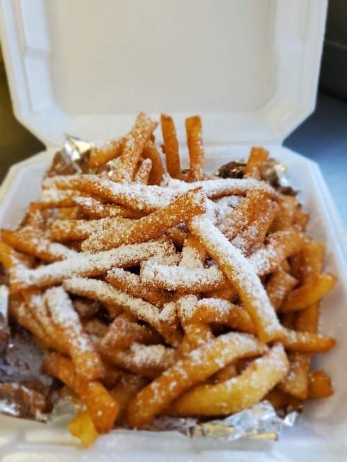 A takeout container filled with golden fries dusted with powdered sugar.