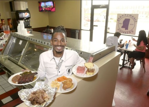 A smiling man holds three plates of food in a restaurant, showcasing a variety of dishes.