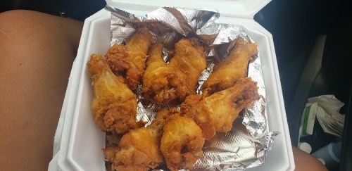 A takeout container filled with crispy fried chicken drumsticks on a foil-lined tray.