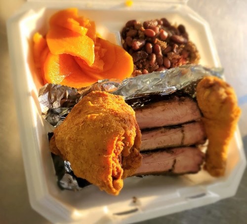 A takeout container with fried chicken, sliced brisket, black beans, and sweet potatoes.