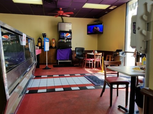Interior of a casual restaurant with a soda machine, tables, and a TV showing a program. Brightly colored decor.