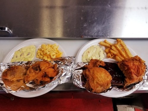 Two plates of food: one with fried chicken, ribs, and macaroni, the other with fried chicken and crinkle-cut fries.