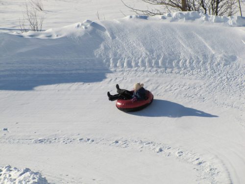 A person in a red snow tube slides down a snowy hill on a bright winter day.