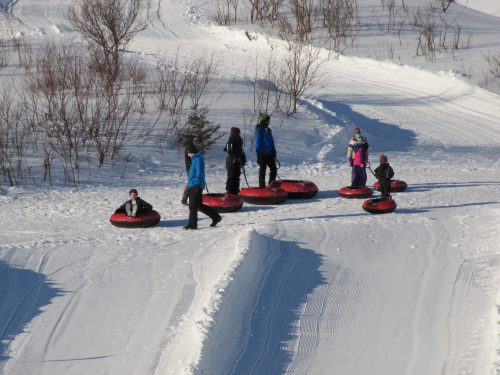 A group of people in winter clothing enjoying tubing on a snowy hill, with several inflatable tubes scattered around.