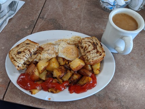 A plate of breakfast with eggs, seasoned potatoes, toast, and a cup of coffee on a table.