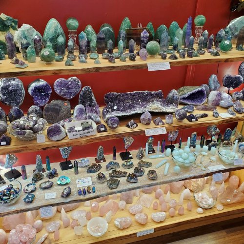 A display of various colorful gemstones and crystals arranged on shelves against a red background.