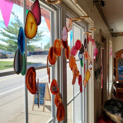 Colorful agate slices hang in a sunny window, creating a vibrant display with various shapes and hues.