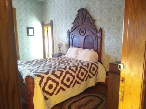 Cozy bedroom featuring a large wooden bed, patterned quilt, and vintage decor against floral wallpaper.