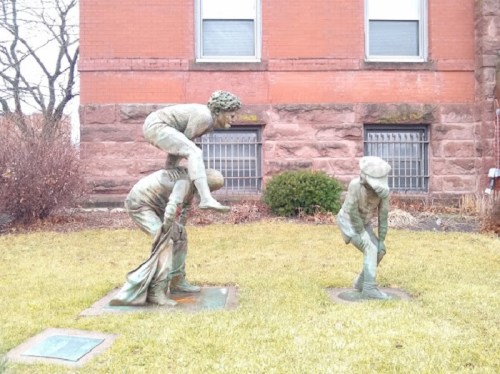 Two bronze sculptures depict children playing: one child on another's back, while a third child bends down.