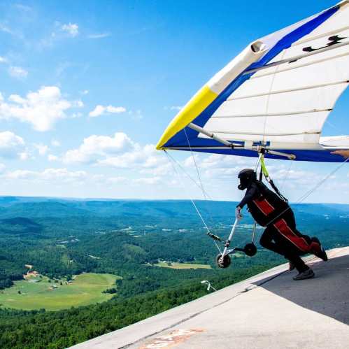 A person in a wingsuit glides over a scenic landscape with green hills and a blue sky.