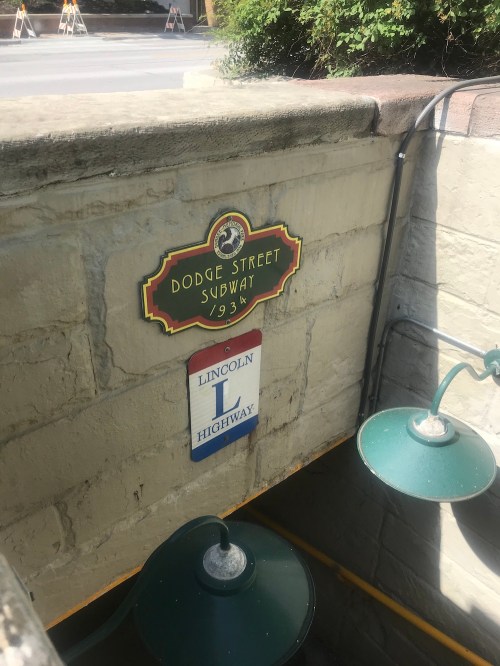 Signage for Dodge Street Subway and Lincoln Highway, mounted on a stone wall near a stairway entrance.