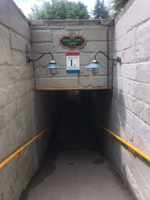 A dimly lit tunnel entrance with signs for Dodge Street and Lincoln Highway, flanked by two green lamps.