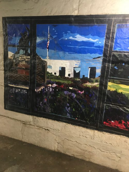Colorful mural depicting a landscape with flowers, a flag, and buildings, set against a blue sky.