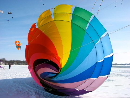 A colorful, spiraled kite in vibrant hues of red, blue, green, and yellow against a snowy landscape.