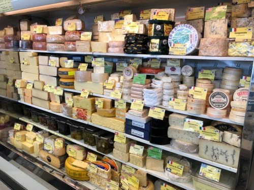 A display case filled with various types of cheese, each labeled with price tags and descriptions.