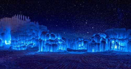 A stunning night scene of illuminated ice formations under a starry sky, glowing in shades of blue.