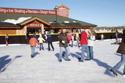 A busy ice skating rink with people skating and enjoying winter activities outside a rental center.