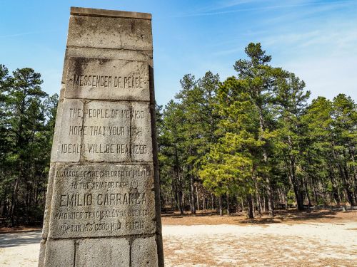 A stone monument inscribed with "Messenger of Peace" in a forested area, surrounded by tall pine trees.
