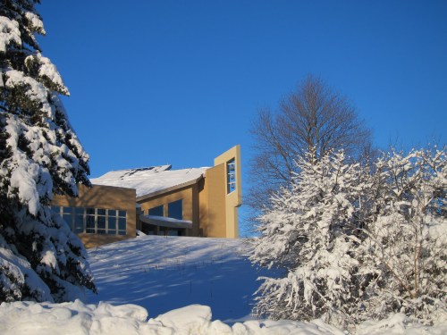 A modern building with a unique design, surrounded by snow-covered trees under a clear blue sky.