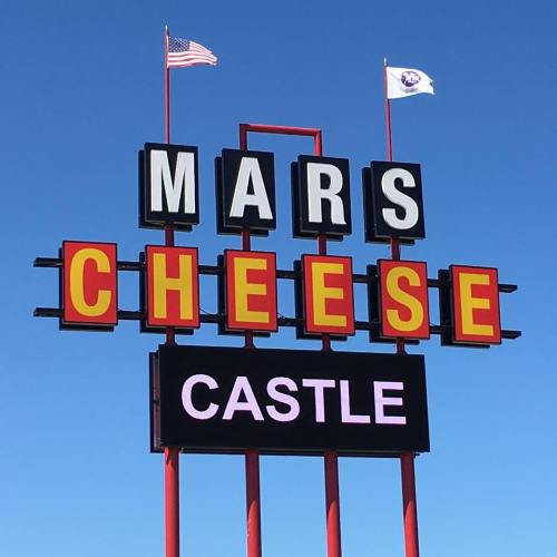 Sign for "Mars Cheese Castle" with American flags against a clear blue sky.